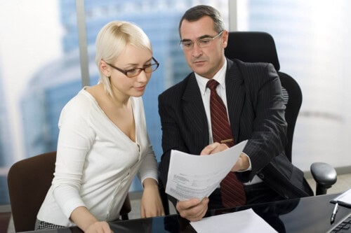 Real estate agent discussing commission dispute with a broker, reviewing contract documents in a professional office setting.